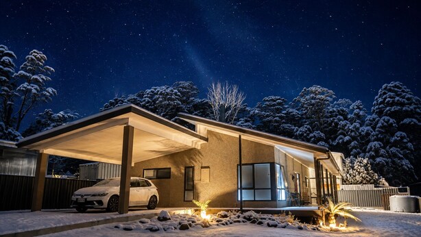 Ett modernt hus med ett garage som har ett tak, en bil parkerad inuti och snö på marken.