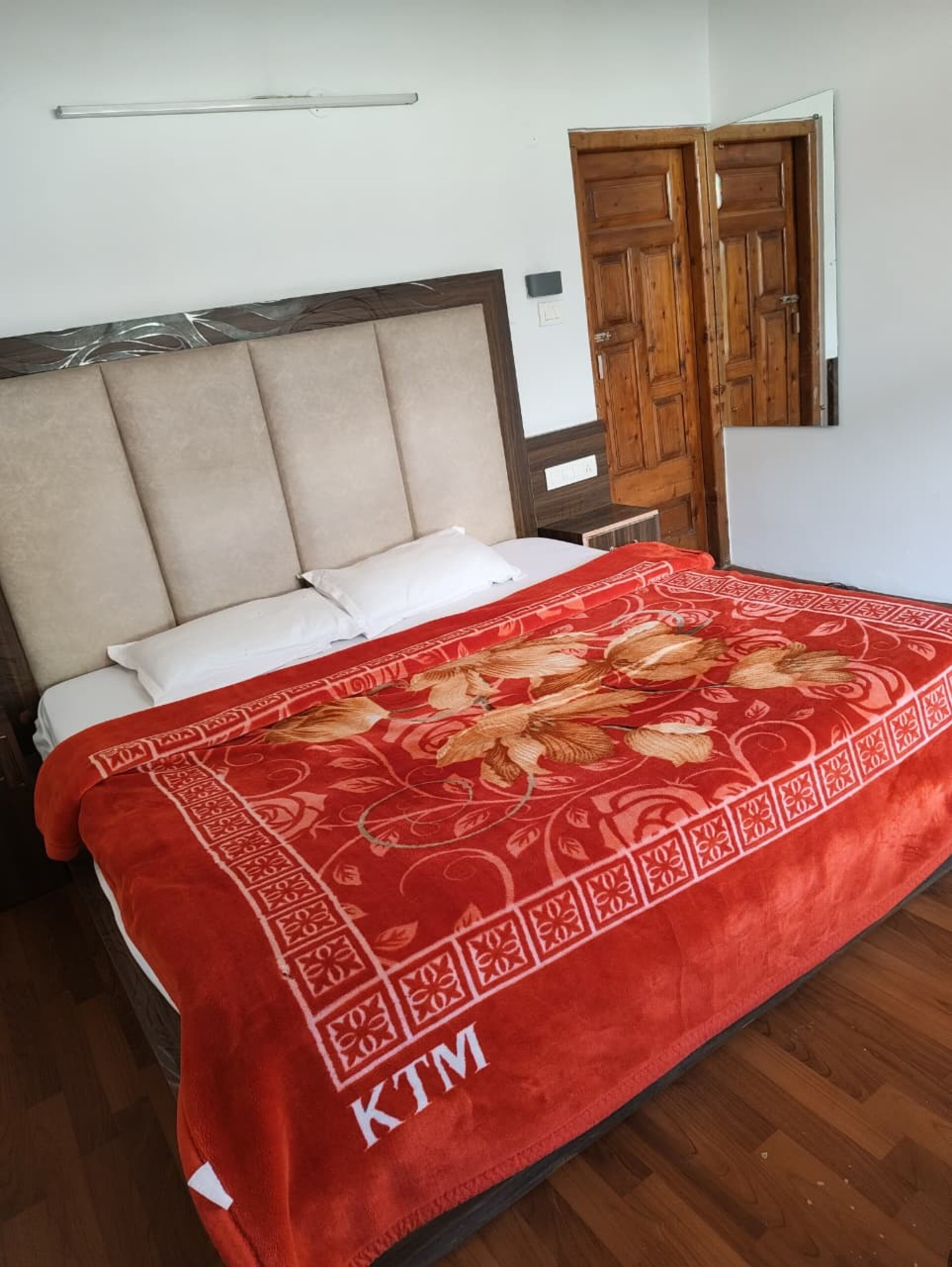 Een bed met een rode deken, een houten hoofdbord en een houten garderobe met spiegel.
