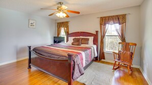 A bedroom with a wooden bed, a ceiling fan, a rocking chair, and a window with curtains. - Stay In peace and rlx (Brevard County)