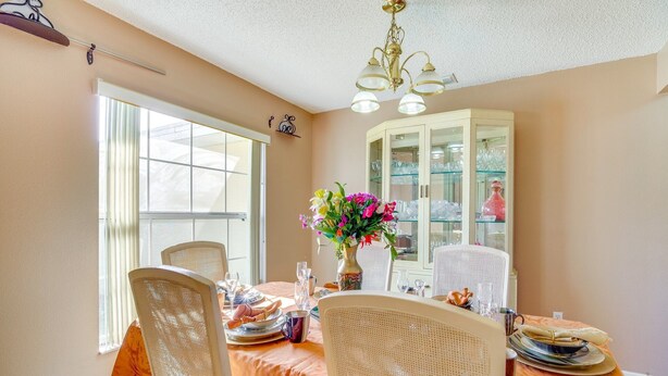 A dining room with a table set for four, a cabinet with glass doors, and a chandelier. - Stay In peace and rlx (Brevard County)