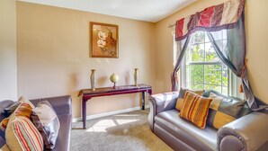 A living room with a sofa, a small table with decorative items, a painting on the wall, and a window with curtains. - Stay In peace and rlx (Brevard County)