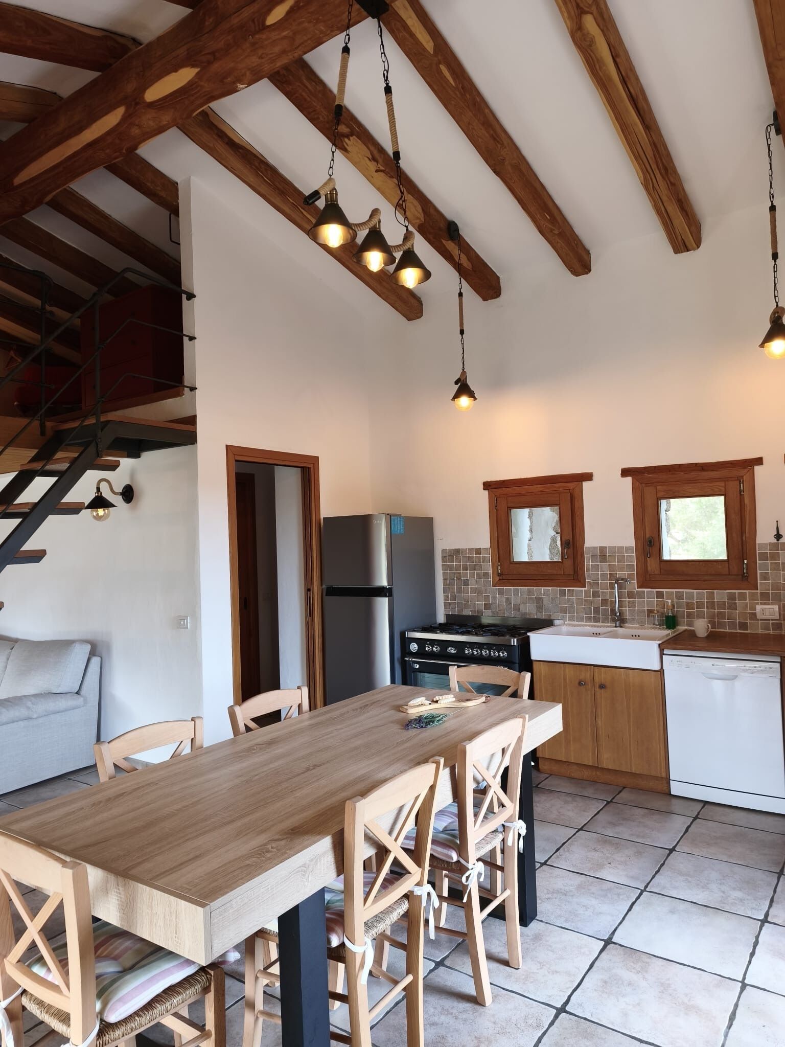Une cuisine avec des poutres en bois, une table à manger, des chaises, un réfrigérateur, une cuisinière et un évier.