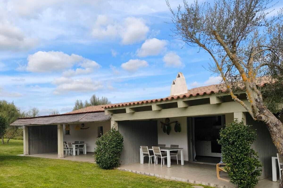 Ein zweistöckiges Haus mit einer Terrasse und einem überdachten Sitzbereich, davor ein Baum.