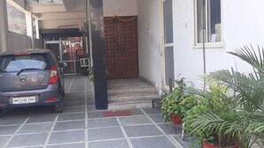A car parked in a narrow driveway leading to a building with a wooden door and steps. - Hotel Shivdham (Lucknow)