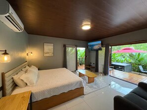 Ein Schlafzimmer mit Bett, Nachttisch und Fernseher. Ein Balkon mit Tisch und Stühlen ist vorhanden.