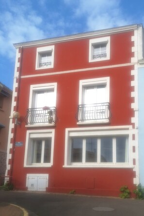 Ein rotes Gebäude mit weißem Zierrat, zahlreichen Fenstern und einem Balkon mit Geländer.
