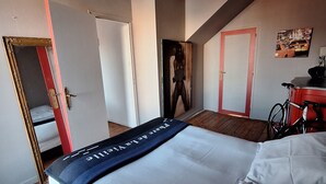 Une chambre d’hôtel avec un lit, un plancher en bois, un miroir à cadre rouge et un vélo dans un coin.