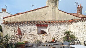 Une cour avec un mur en pierre, une petite fenêtre, des plantes en pot et une table avec des chaises.