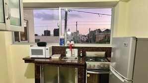 Una cocina con microondas, estufa, refrigerador y ventana con vista a la ciudad.