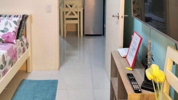 Ein kompakter Wohnraum mit Bett, Schreibtisch mit Computer, Fernseher und Kühlschrank.