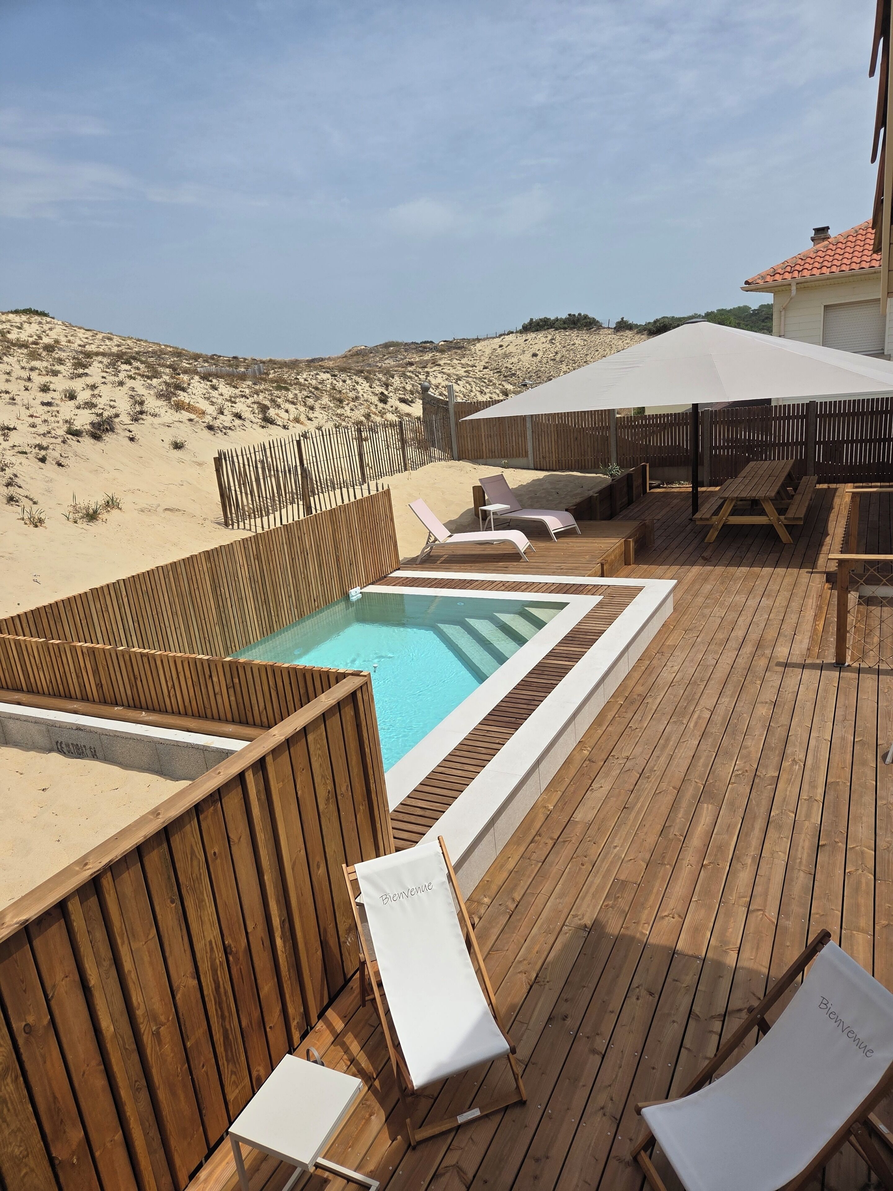 A wooden deck with a hot tub, lounge chairs, and a pool.
