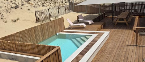 A wooden deck with a hot tub, lounge chairs, and a pool.