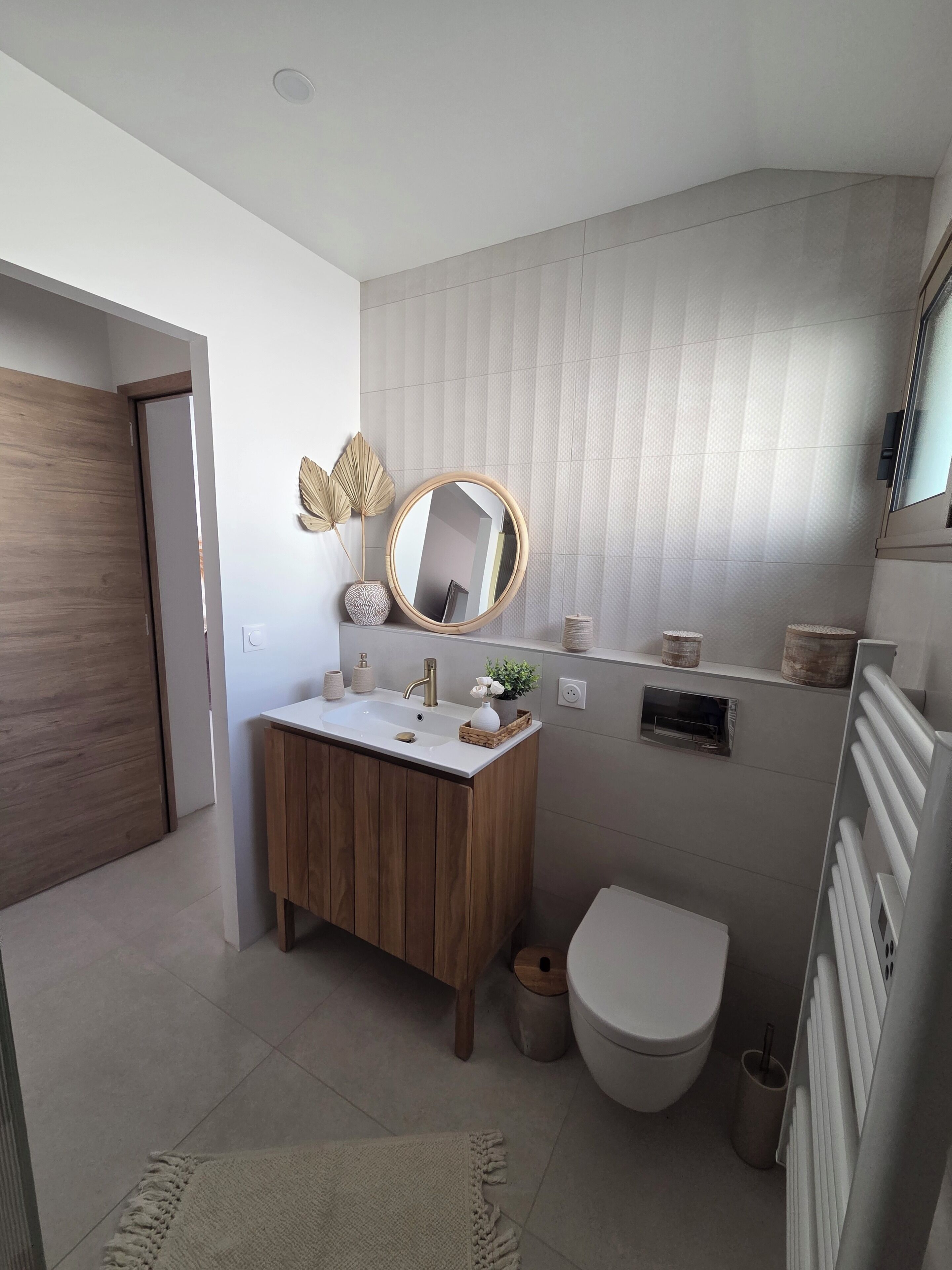 Une salle de bain moderne avec un meuble-lavabo en bois, un miroir rond, des toilettes et un radiateur.