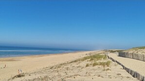 A beach with a wooden fence, sandy dunes, and a clear blue sky.