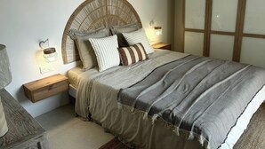 A bed with a woven headboard, bedside lamps, and a striped throw blanket.