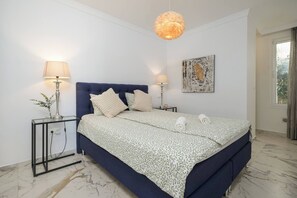 Ein Schlafzimmer mit einem Bett, zwei Nachttischen, einer Pendelleuchte, einem Wandbild und einem Fenster.