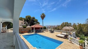 Una piscina en la azotea con vistas a la ciudad, una zona de estar cubierta y una palmera.