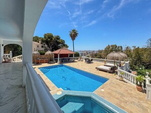 Ein Pool auf dem Dach mit Blick auf die Stadt, eine überdachte Lounge und eine Palme.
