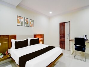 A hotel room with a bed, bedside table, lamp, desk, chair, and framed artwork on the wall.
