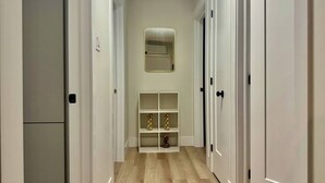 Un couloir étroit avec des portes blanches, un miroir au mur et une étagère ornée d’objets décoratifs.