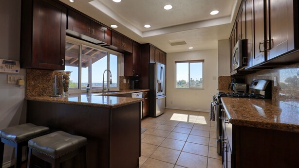 A modern kitchen with dark wood cabinets, granite countertops, stainless steel appliances, and a large island with bar stools. - San Diego Hilltop Haven: Game Room+Views! 18 Minutes from Downtown (Spring Valley)