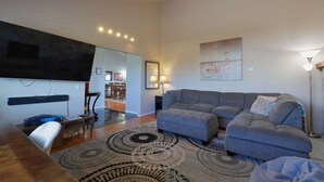 A modern living room with a sofa, ottoman, and a television mounted on the wall. - San Diego Hilltop Haven: Game Room+Views! 18 Minutes from Downtown (Spring Valley)