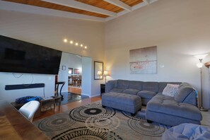 Un salon moderne avec un canapé, un pouf et un téléviseur fixé au mur.