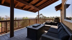 A covered outdoor area with a wooden deck, a black table, a sofa, and a view of the landscape. - San Diego Hilltop Haven: Game Room+Views! 18 Minutes from Downtown (Spring Valley)