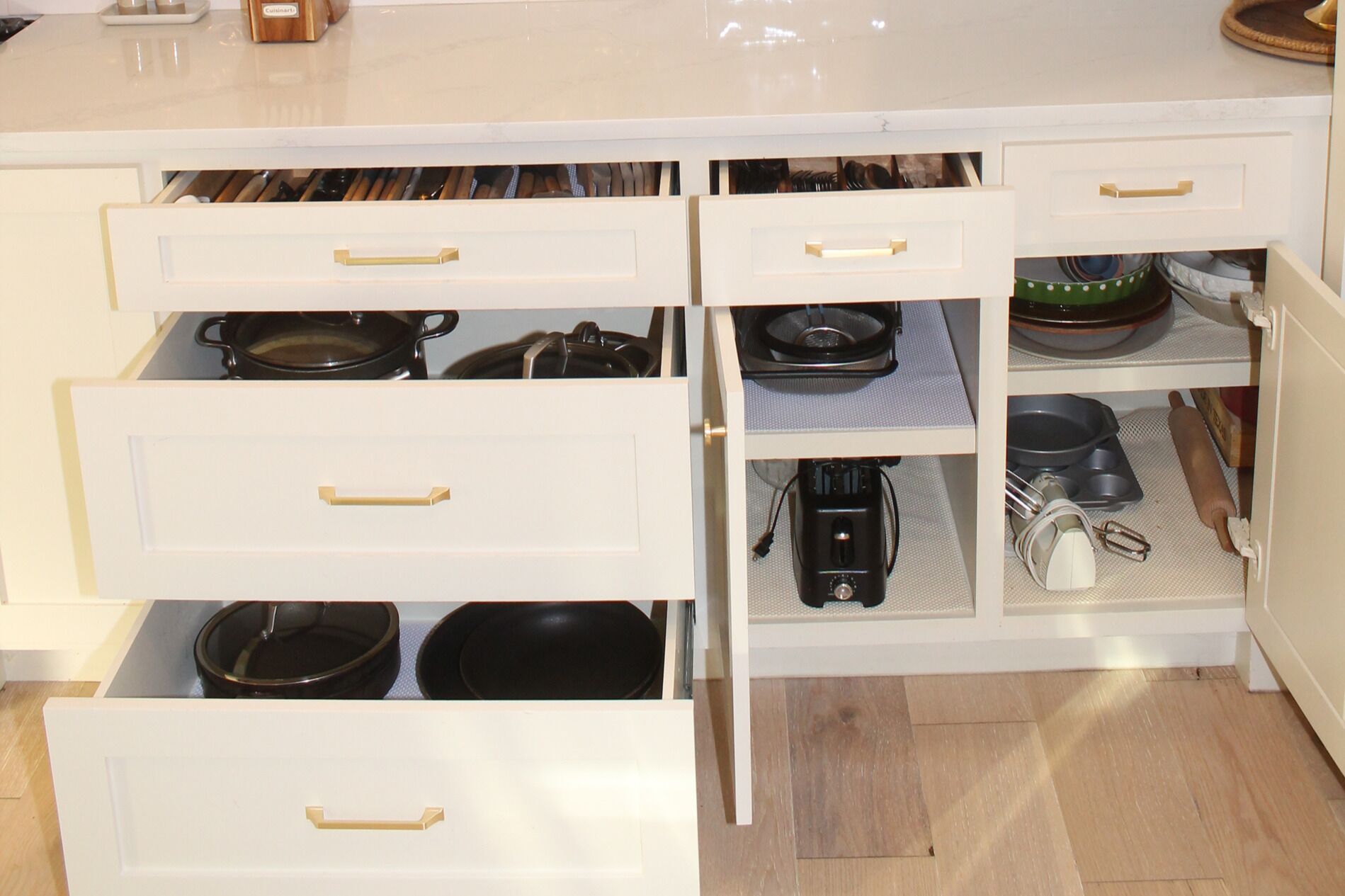A kitchen with white cabinetry, multiple drawers, and various kitchen utensils and appliances.