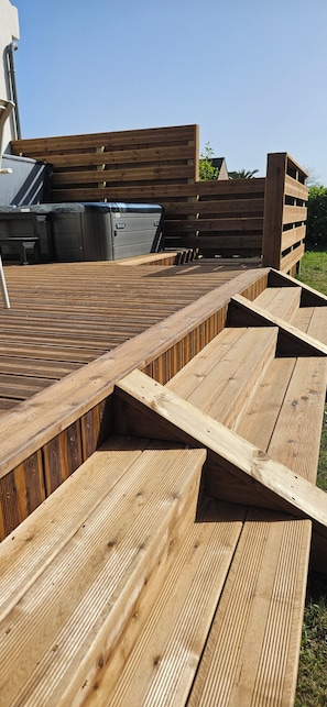 A wooden deck with steps leading to a covered area, a trash bin, and a grill. - House 3bed Terraces Jacuzzi Garden 4min from the beach. (Cléder)