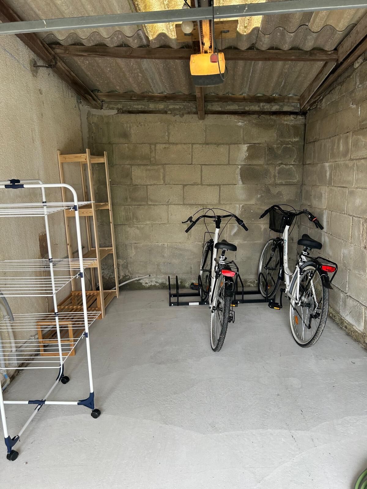 A garage with two bicycles, a metal drying rack, and a wooden ladder.