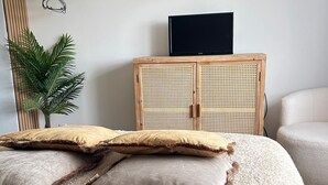 A bedroom with a bed, a rattan cabinet, a television, and a plant.