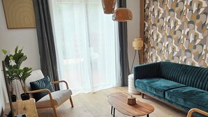 A modern living room with a sofa, coffee table, and chairs. There is a plant, a lamp, and a wall with a geometric pattern.
