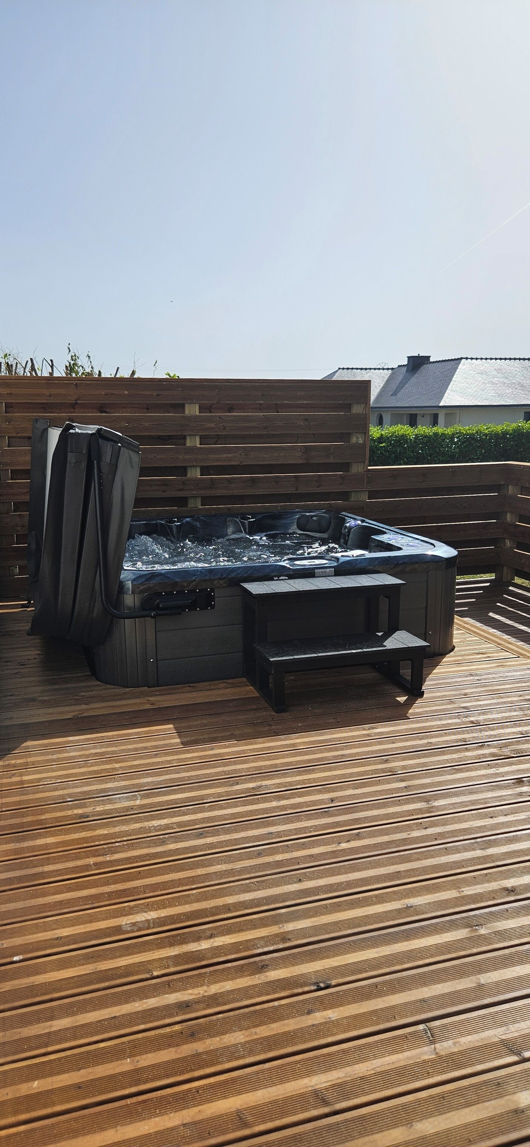 A hot tub on a wooden deck with a wooden fence and a building in the background.