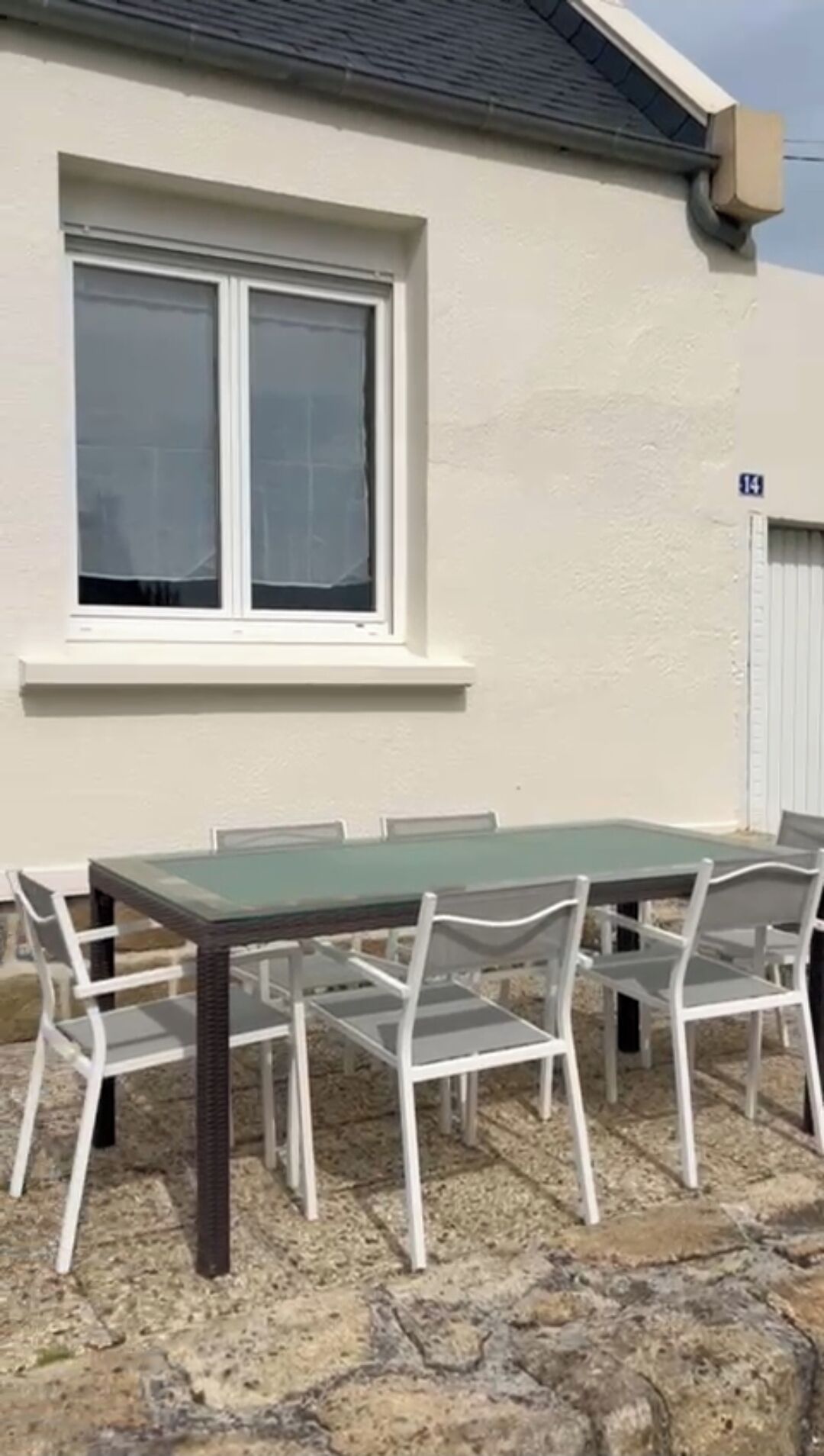 Un edificio con un amplio ventanal, un cartel con el número 14, y una mesa con sillas en el exterior.