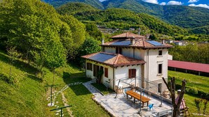 Un edificio de dos plantas con tejado de baldosas, paneles solares y un patio con mobiliario exterior.