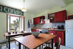 Une cuisine avec des placards rouges, un fourneau et un coin repas comprenant une table et des chaises.