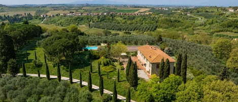A villa with a tiled roof, surrounded by olive groves and a swimming pool.