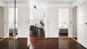 Una habitación de hotel moderna con piso de madera, una zona de comedor con una mesa redonda y sillas, y una cama con cabecera gris.