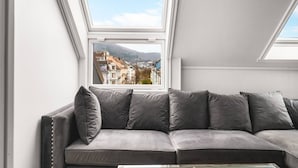 Una sala de estar moderna con un sofá gris, vista de edificios a través de un tragaluz y una pared blanca.