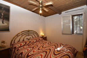 Ein Schlafzimmer mit Bett, Deckenventilator, Fenster und einem Gemälde an der Wand.
