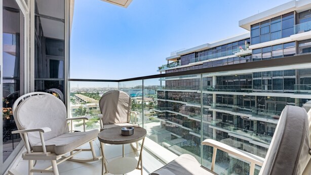 Ein Balkon mit Blick auf eine Stadtlandschaft, möbliert mit einem Schaukelstuhl, einem kleinen Tisch und einer Couch.