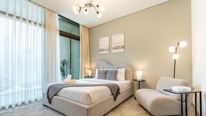 Ein modernes Hotelzimmer mit einem großen Bett, einem Nachttisch mit Lampe, einem Sessel und einem Bild an der Wand.