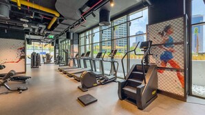 Ein Fitnessstudio mit Laufbändern, Krafttrainingsgeräten und einem großen Fenster mit Blick auf die Stadt.