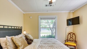 Un dormitorio con una cama, una ventana, una silla y una televisión instalada en la pared.