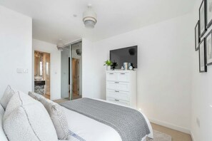 A bedroom with a bed, a dresser, a TV, and a door leading to another room. - 2-Bedroom Bermondsey Apartment (London)