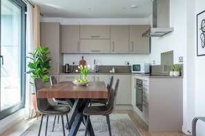 A modern kitchen with a dining table, chairs, and a potted plant. - 2-Bedroom Bermondsey Apartment (London)
