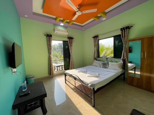 Un dormitorio con cama, televisión, ventilador de techo y ventana con cortinas.