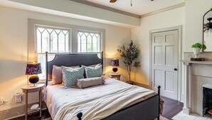 Una camera da letto con un letto, due comodini, un tavolino, un camino e una finestra vista alberi.