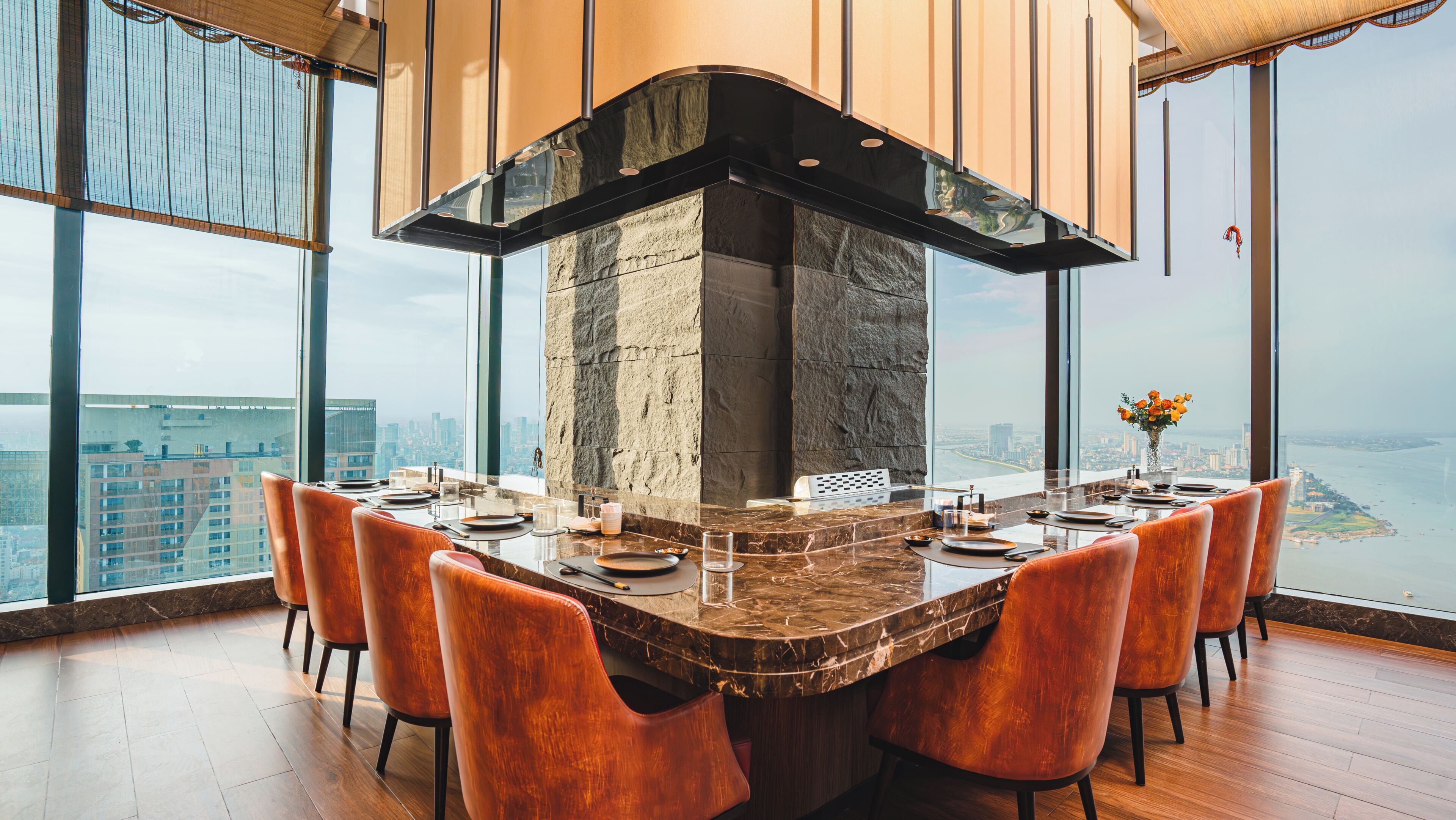 A high-rise restaurant with a large stone fireplace, a panoramic city view, and modern seating.